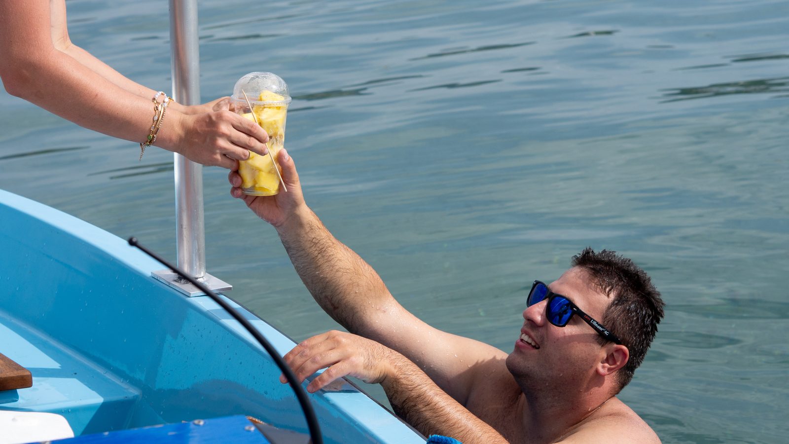 Ein frisch geschnittener Ananasbecher wird vom Seekiosk direkt an einen Schwimmer im Bodensee übergeben